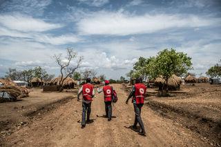 Three men walking in an open space surrounding by dirt paths 和 huts 